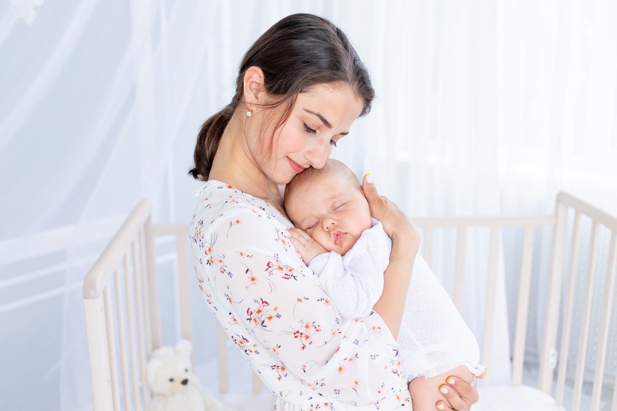 a young mother holds a newborn baby in her arms and puts it to sleep in the bedroom near the crib, the concept of motherhood and a happy family, baba, kisbaba, altatás, ringat