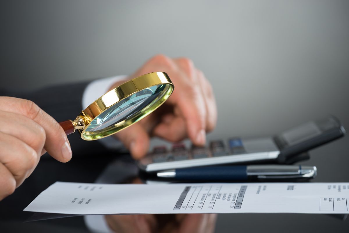 Close-up,Of,Businessman,Hand,Inspecting,Invoice,With,Magnifying,Glass,And